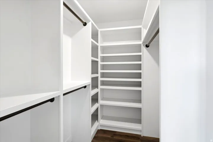 Built-in closet system with white shelving, multiple hanging rods, and wood-finish flooring