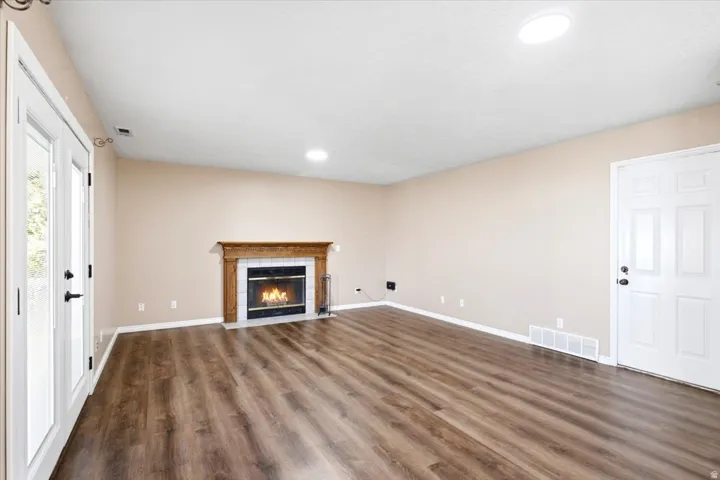 Spacious room featuring wood-finish flooring, a fireplace with a wood mantel, recessed lighting, and French doors