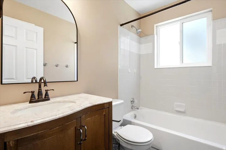 Curved wood-finish vanity with a light-toned countertop, under-mount sink, and bronze-finish faucet