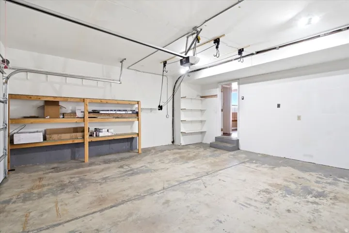 Garage space featuring a concrete floor, built-in shelving, a garage door opener, and a doorway with steps