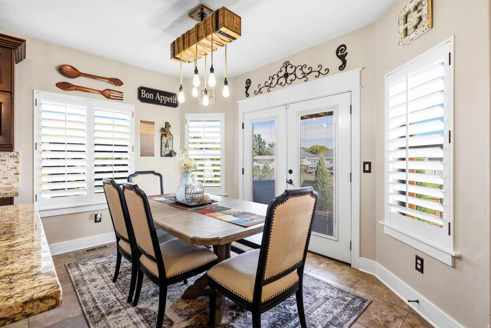 Dining area featuring a wood-plank style dining table and decorative chandelier with Edison bulbs, French doors and plantation shutters.