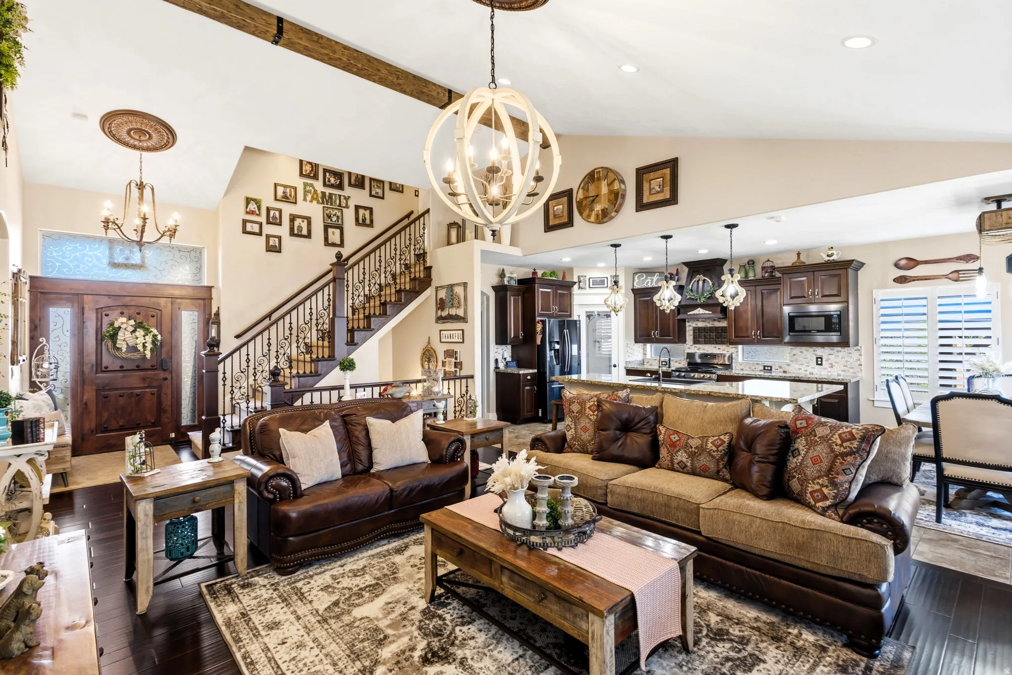 Vaulted ceiling with exposed wood beams, dark wood-finish flooring, staircase with ornate iron balusters, kitchen with dark wood cabinetry, and black stainless-steel appliances