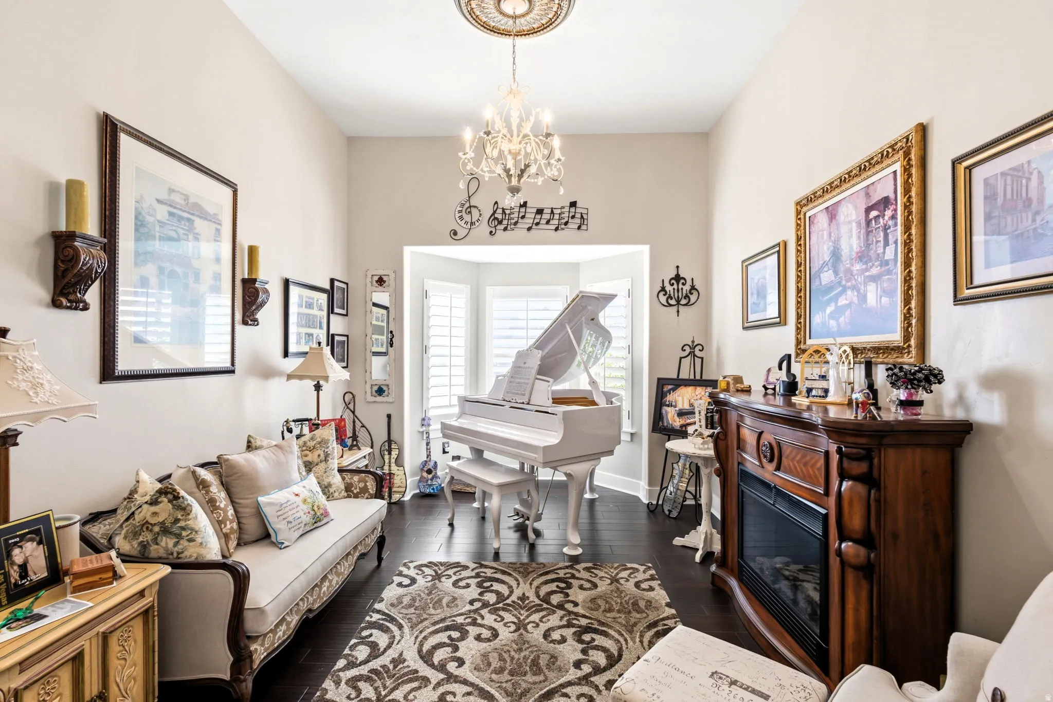 Formal living room, recessed bay window, dark wood-finish flooring, free standing fireplace with wood mantel, decorative ceiling medallion, and crystal chandelier