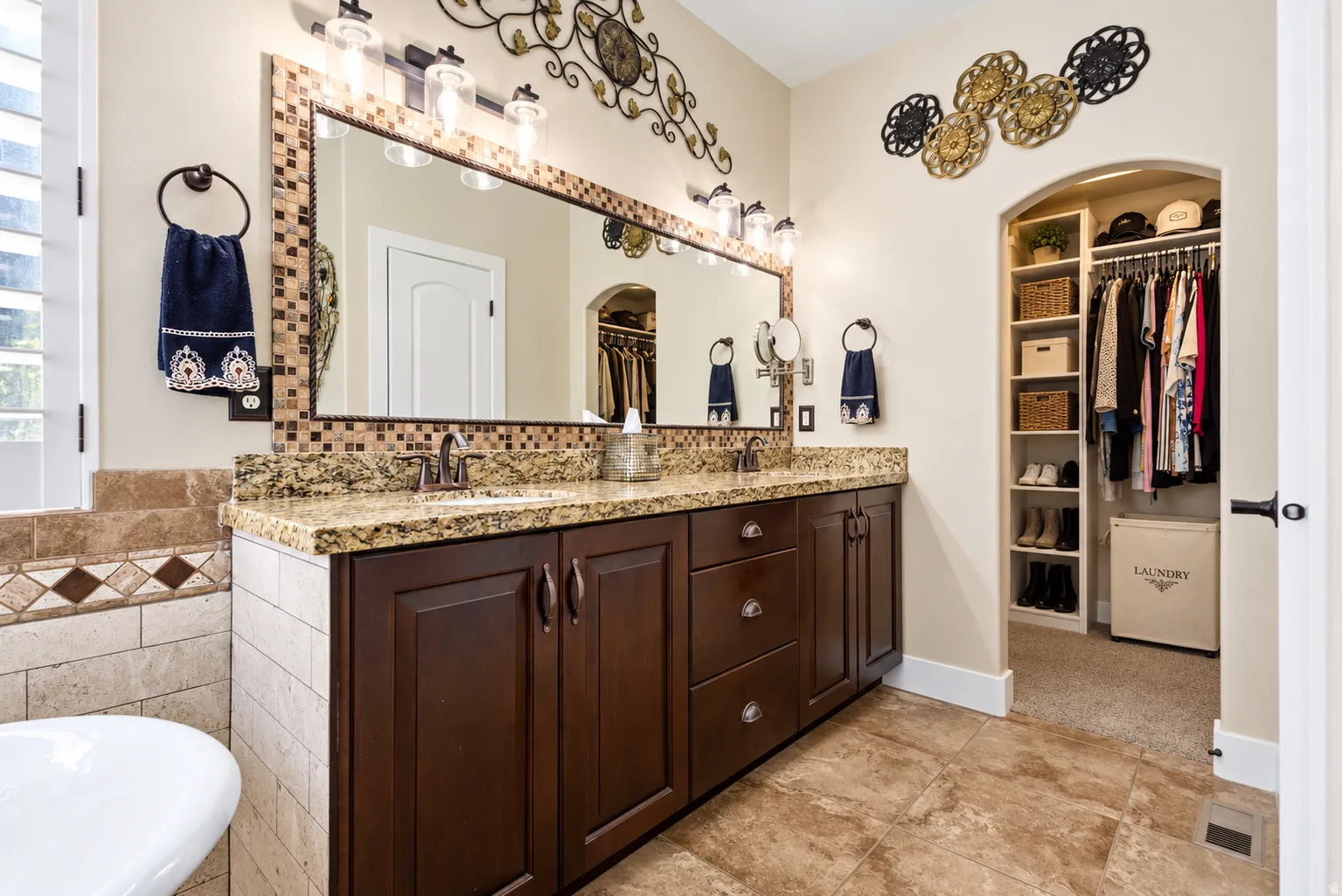 Primary bath, double vanity with granite countertop, dark wood-finish cabinetry, and mosaic tile backsplash