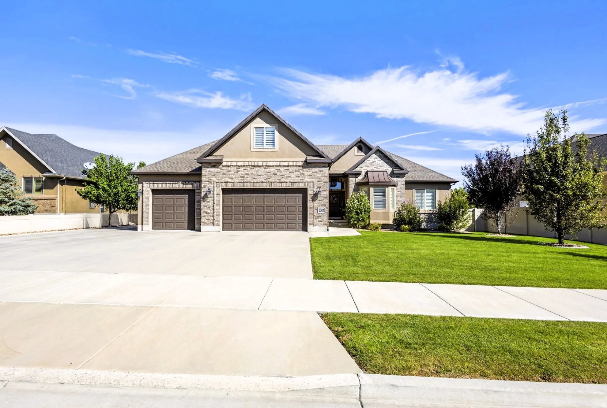 Stone and stucco exterior, three-car garage, concrete driveway, and a front lawn with mature fruit trees