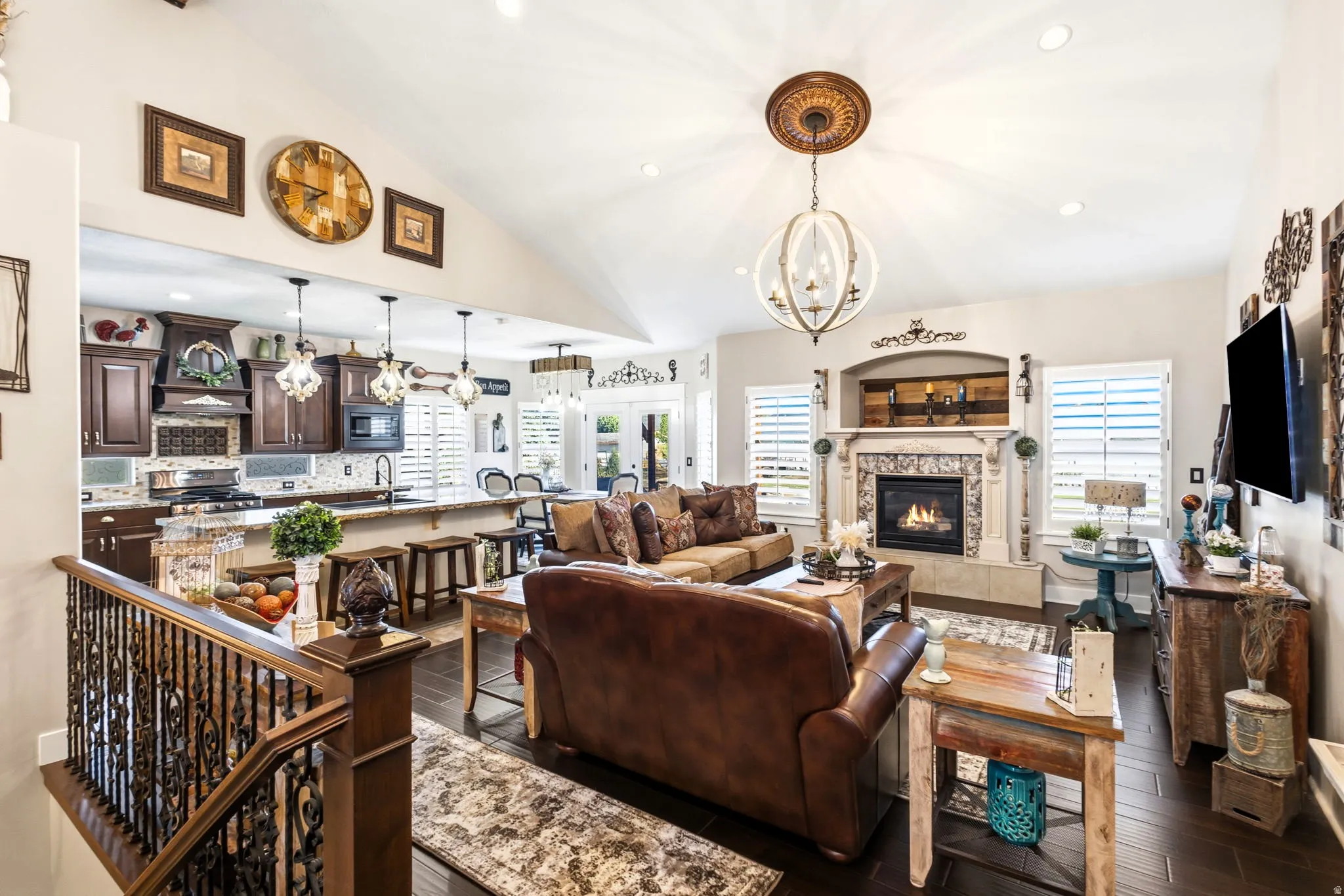 Vaulted ceiling living area with fireplace featuring a decorative mantel, wood-finish flooring, and a kitchen with dark wood cabinetry and a granite countertop