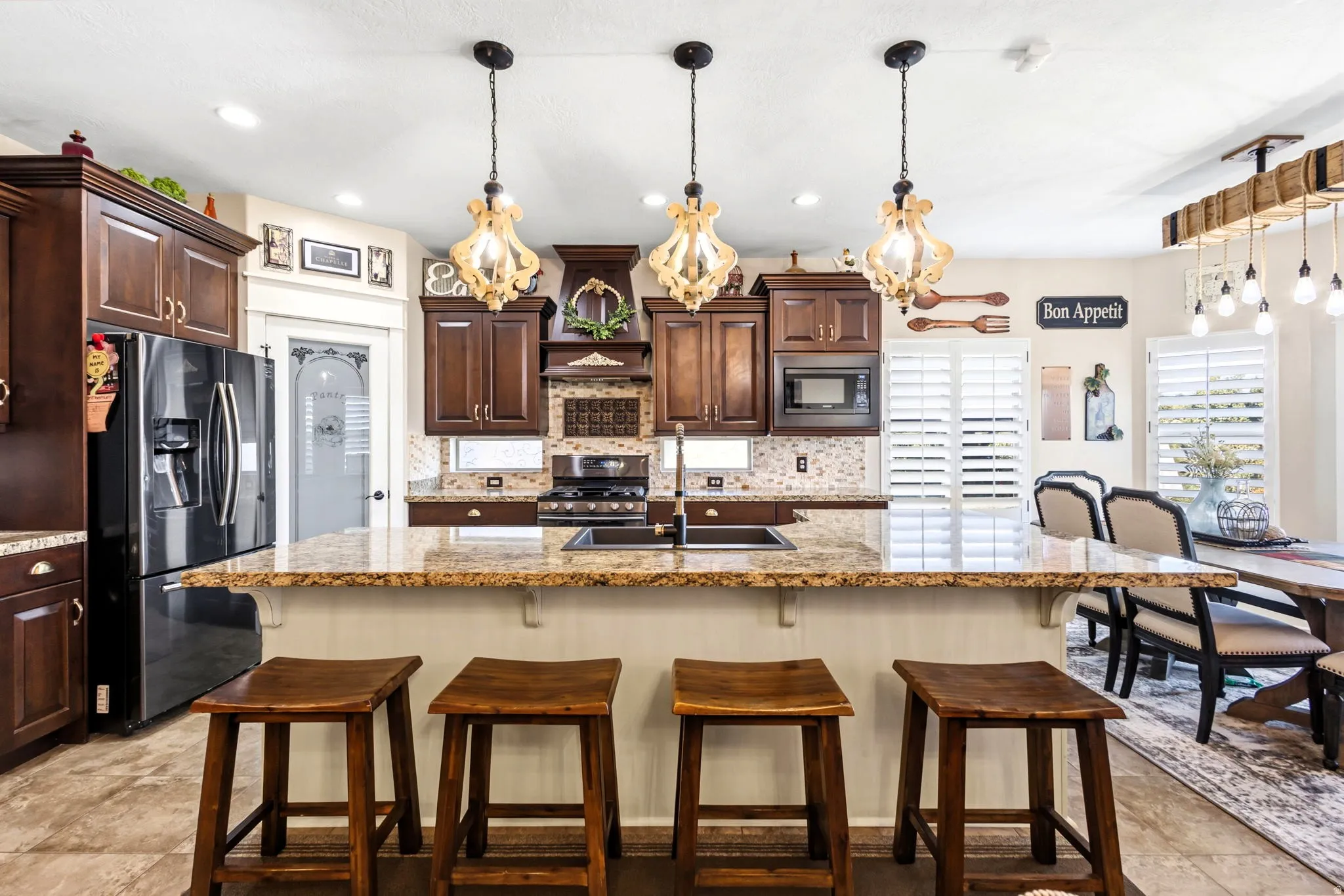 Spacious kitchen island with seating, dark wood cabinetry, integrated black stainless appliances, and decorative pendant lighting