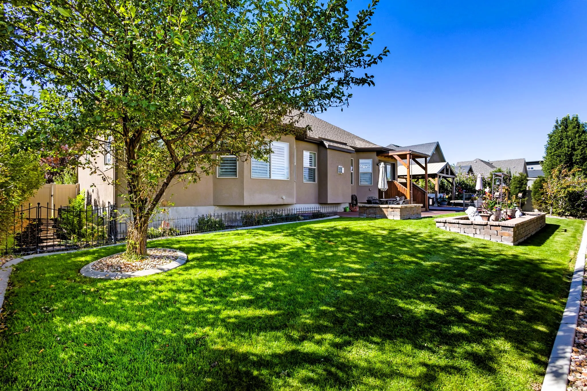 Expansive manicured lawn with a mature shade tree and decorative rock bed