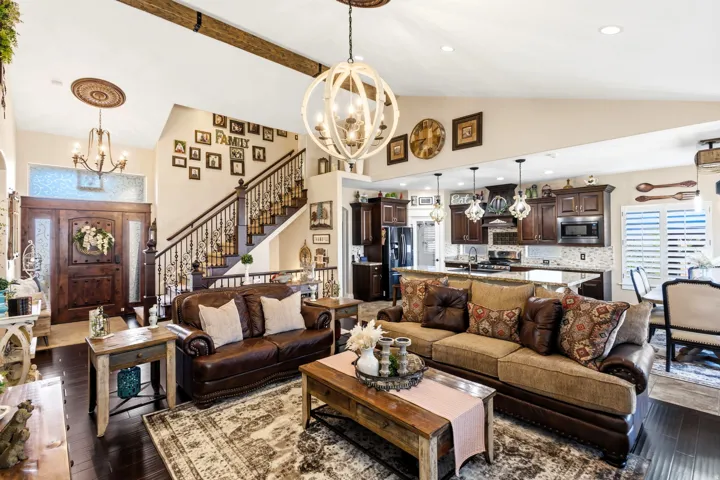 Vaulted ceiling with exposed wood beams, dark wood-finish flooring, staircase with ornate iron balusters, kitchen with dark wood cabinetry, and black stainless-steel appliances