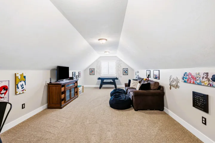 Upstairs oversized carpeted bonus room, featuring sloped ceilings, recessed lighting, and a window with plantation shutters