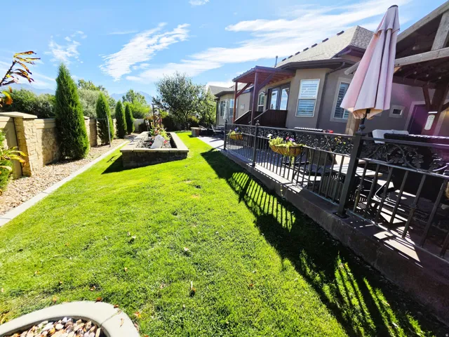 Manicured lawn, elevated patio with decorative railing, stone-clad retaining wall, mature perimeter trees, and built-in planters