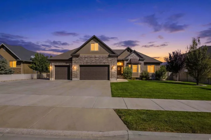 Stone and stucco exterior featuring a gabled roofline, three-car garage, established front yard with a manicured lawn, and concrete driveway