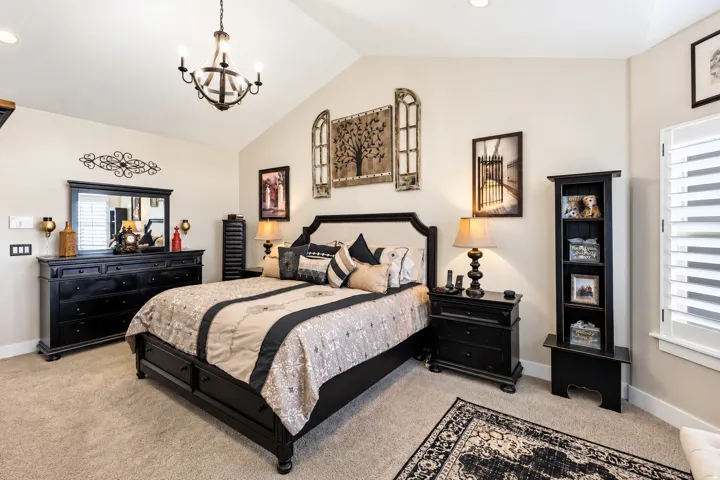 Primary bedroom, vaulted ceiling with an iron chandelier, light-toned walls, recessed lighting, and window with white plantation shutters