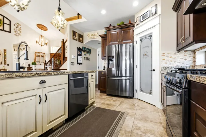Gourmet kitchen featuring granite countertops, black stainless steel appliances, tile backsplash, and a decorative pantry door