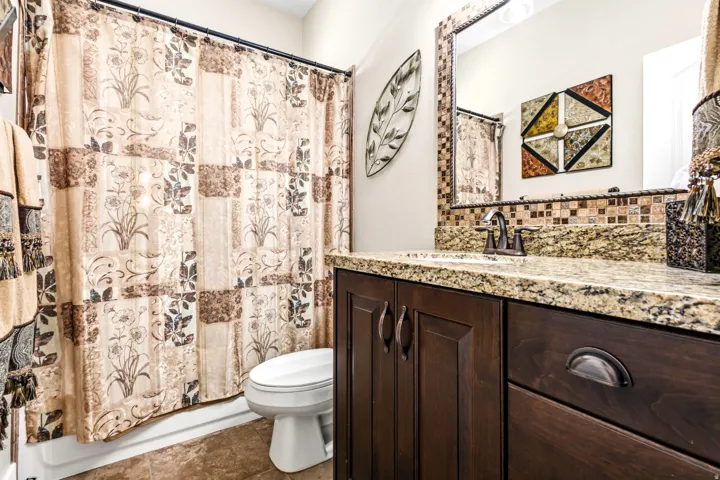Granite vanity countertop with an undermount sink, mosaic tile backsplash, and dark wood-finish cabinetry featuring bronze hardware