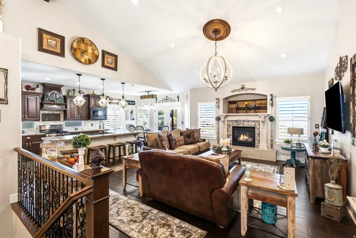 Vaulted ceiling living area with fireplace featuring a decorative mantel, wood-finish flooring, and a kitchen with dark wood cabinetry and a granite countertop