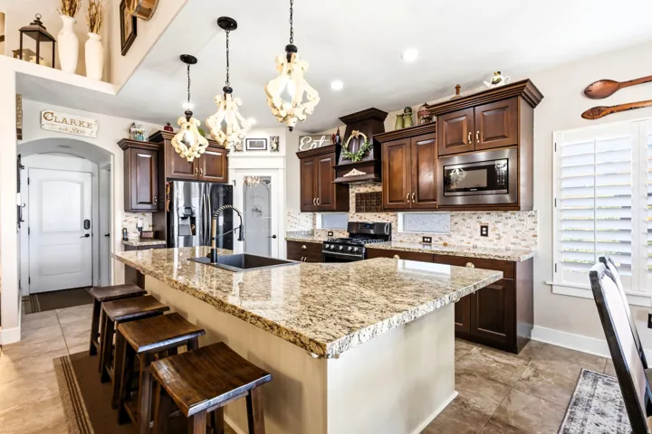 Spacious kitchen featuring an expansive center island with seating, dark wood-finish cabinetry, black stainless steel appliances, and a mosaic tile backsplash