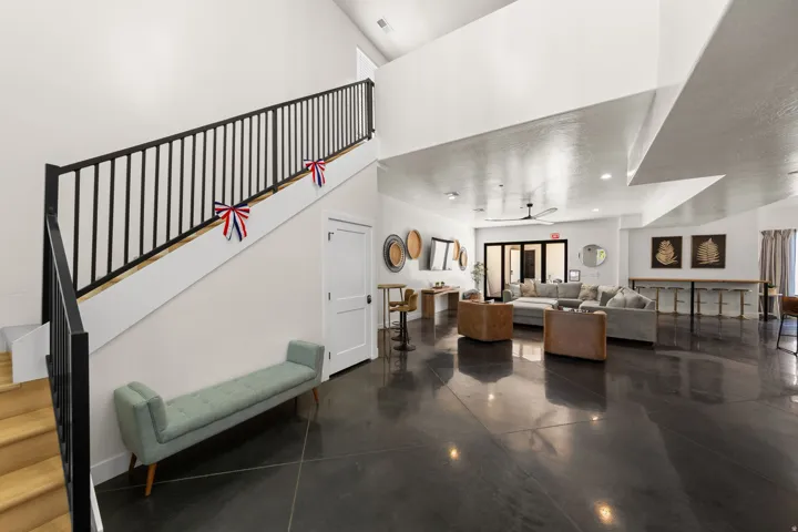 Soaring ceilings with recessed lighting, dark polished concrete flooring, a multi-pane glass door, and a staircase with a black metal railing