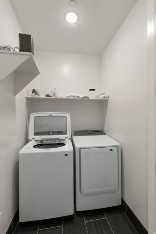 Recessed ceiling lighting illuminates a dedicated laundry space with dark wood-finish tile flooring and crisp white walls