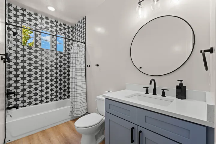 Bathroom featuring a tub and shower combination with patterned wall tile, a window, a single vanity with a white countertop, and wood-finish flooring