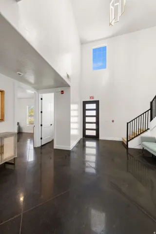 Polished concrete flooring, high ceilings, contemporary light fixture, modern entry door with horizontal lites, and open staircase with metal railing