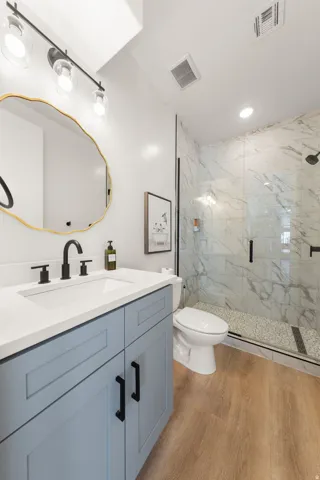 Walk-in shower with glass enclosure, light-toned wood-finish flooring, blue vanity with white countertop, and contemporary black fixtures