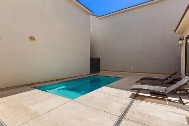 Private courtyard featuring a rectangular swimming pool, concrete patio, and exterior wall sconce