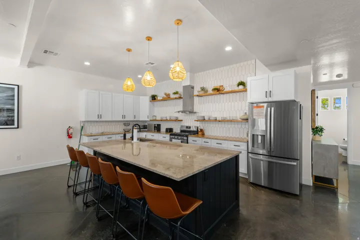 Expansive kitchen island with a stone countertop, white upper and lower cabinetry, stainless steel appliances, and a decorative tile backsplash