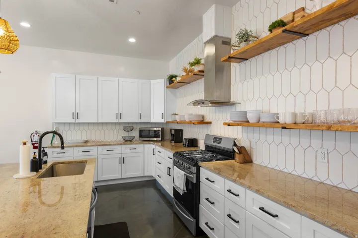 White shaker cabinetry, light-toned countertops, geometric pattern backsplash, stainless steel appliances, and open shelving