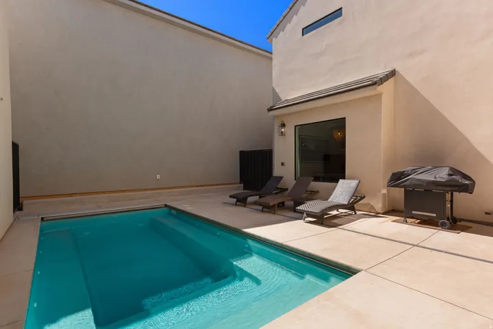 Private backyard featuring a swimming pool with integrated steps, concrete patio, and stucco exterior walls
