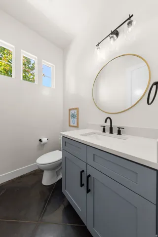 Powder room featuring a gray shaker vanity, white countertop, black hardware, black matte faucet, and an oval gold-framed mirror
