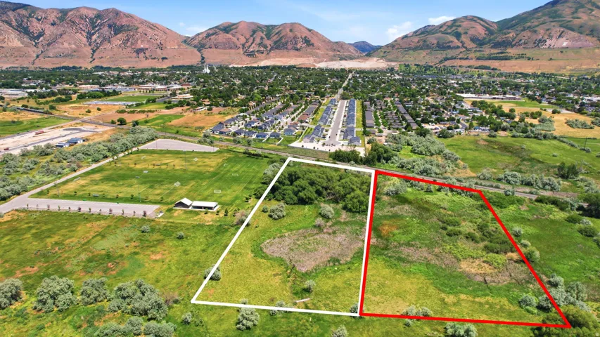 Expansive land parcel with surrounding green space, bordered by mature trees and distant mountainous terrain
