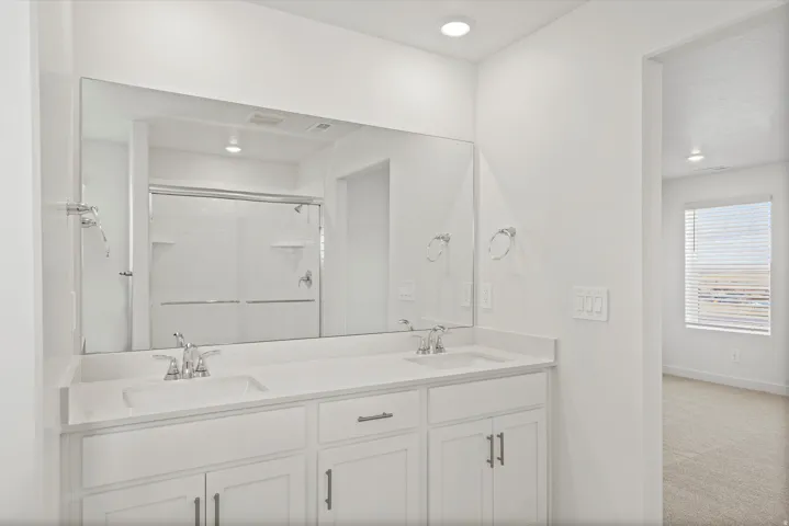 **DISCLAIMER** Interior package may vary. Dual vanity with integrated sinks and chrome fixtures, large wall-mounted mirror, white shaker-style cabinetry with chrome hardware, recessed lighting, and a walk-in shower with tiled walls and sliding glass doors