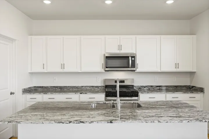 **DISCLAIMER** Interior package may vary. Kitchen featuring a spacious island with a double basin sink, white cabinetry with brushed nickel hardware, and dark patterned countertops