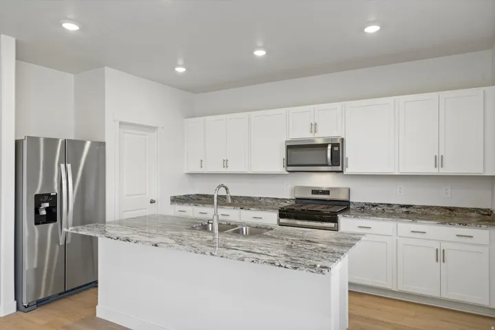 **DISCLAIMER** Interior package may vary. Kitchen featuring an island with a stainless steel sink and a gooseneck faucet, white cabinetry, stainless steel appliances, and recessed lighting