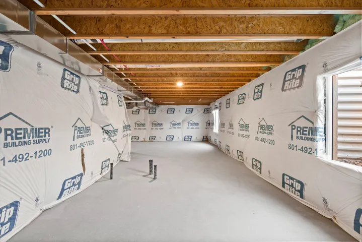 Unfinished basement with exposed ceiling joists, concrete flooring, small windows, and visible ductwork