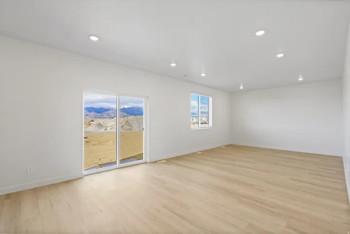 **DISCLAIMER** Interior package may vary. Spacious room featuring light wood-finish flooring, recessed lighting, white walls, a large window, and a sliding glass door