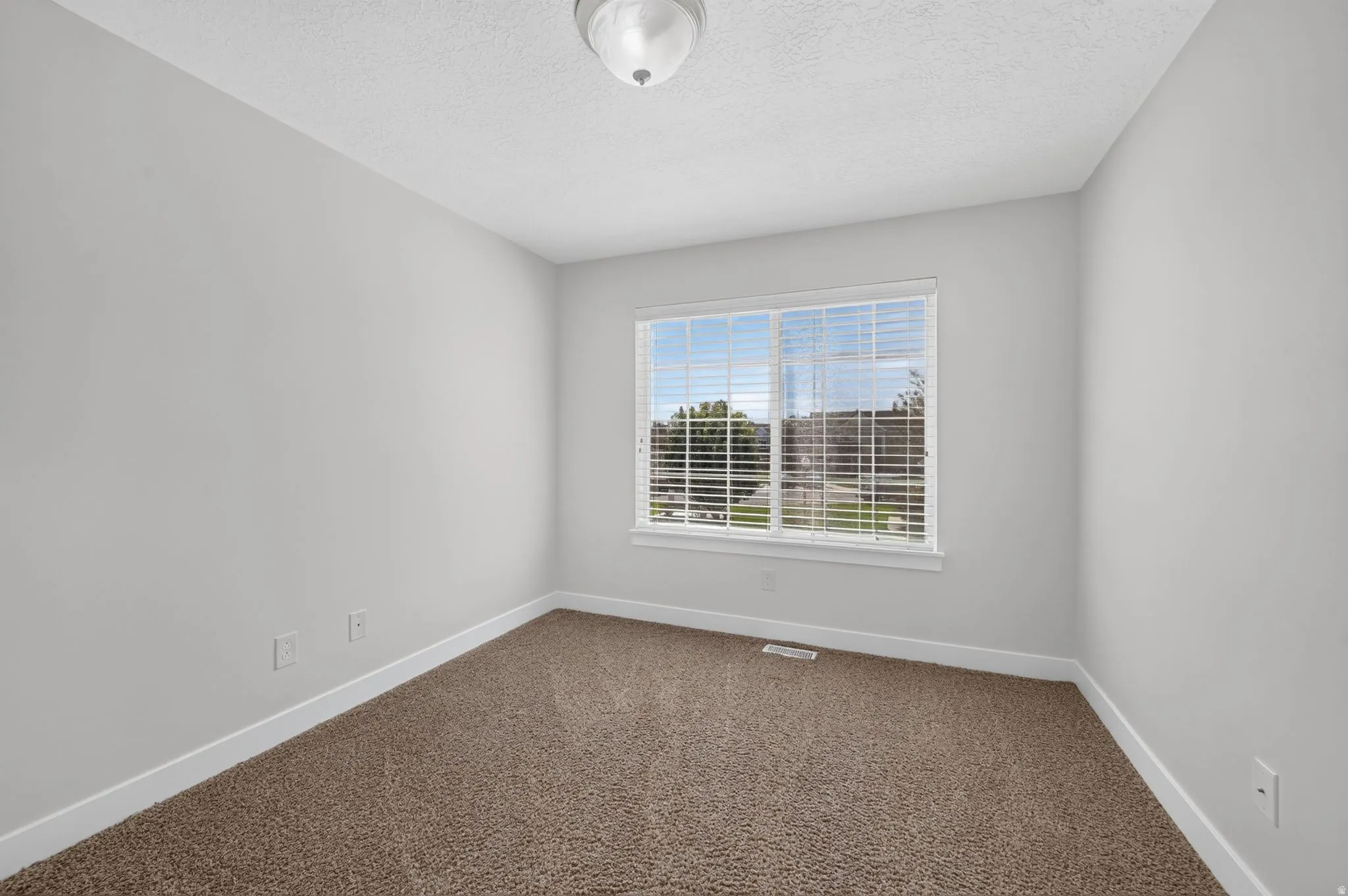 Bright corner bedroom with expansive windows framing natural light, neutral wall finishes, and soft carpeting throughout