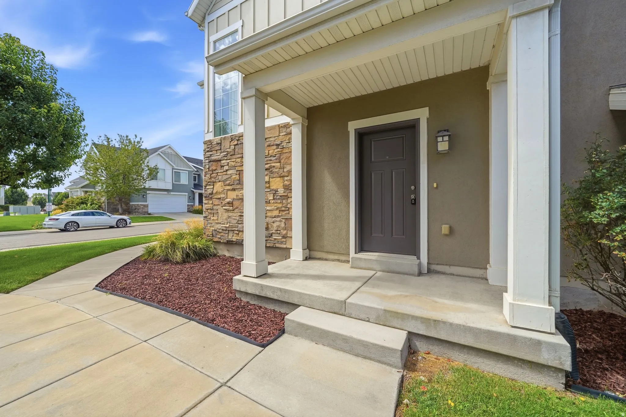 Stucco exterior with stone veneer accents, covered entry, front porch with square columns, and a concrete pathway
