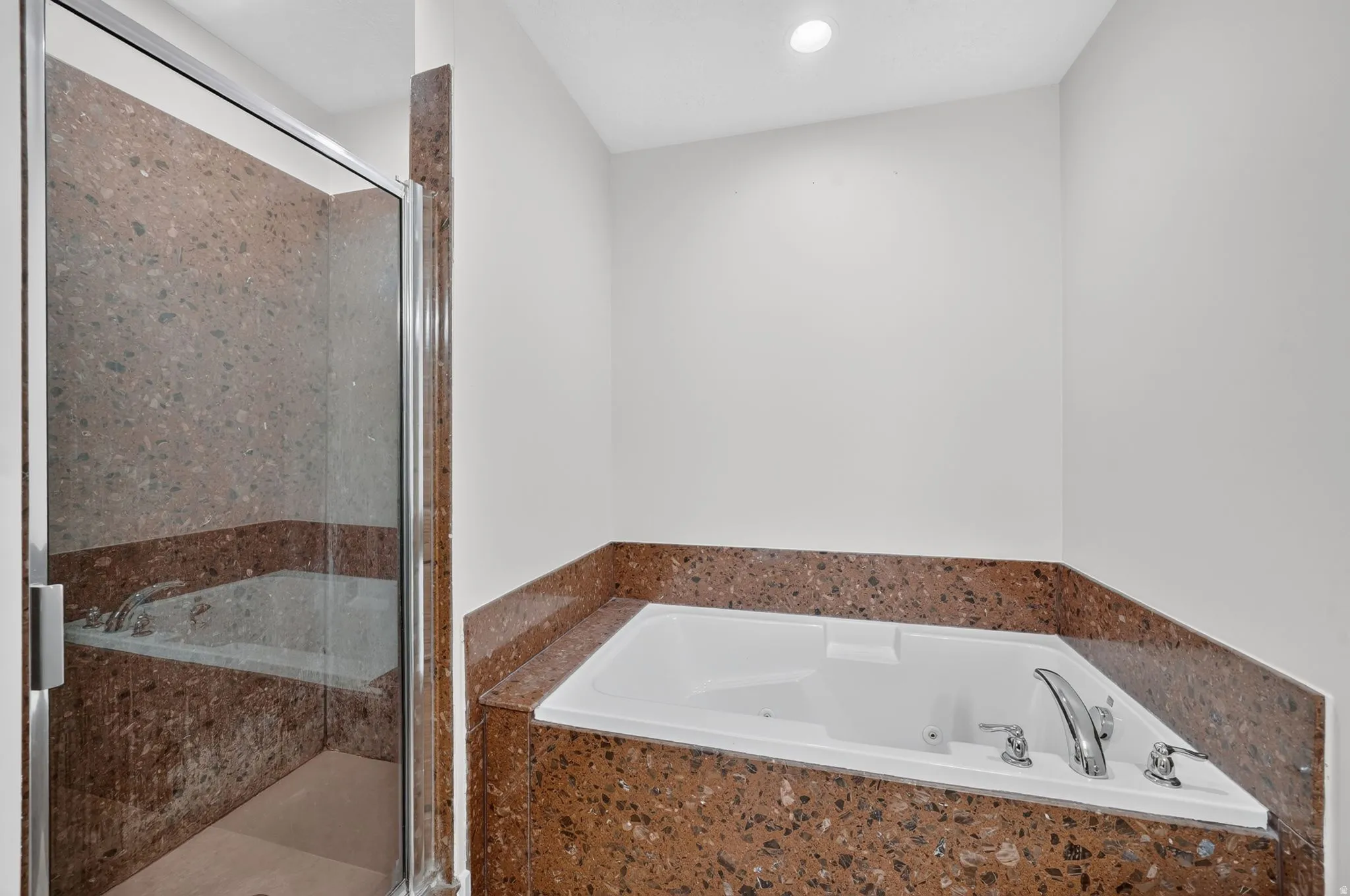 Walk-in shower with clear glass enclosure, a built-in jetted tub, and matching stone finishes