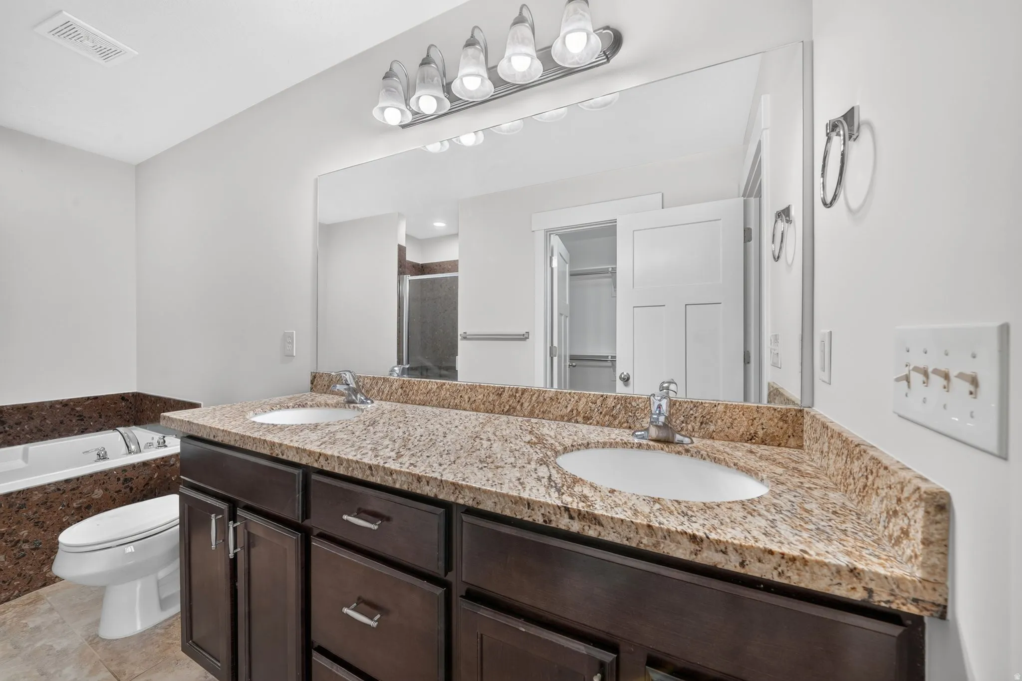 Dual vanity with a stone countertop, dark wood-finish cabinetry, and undermount sinks