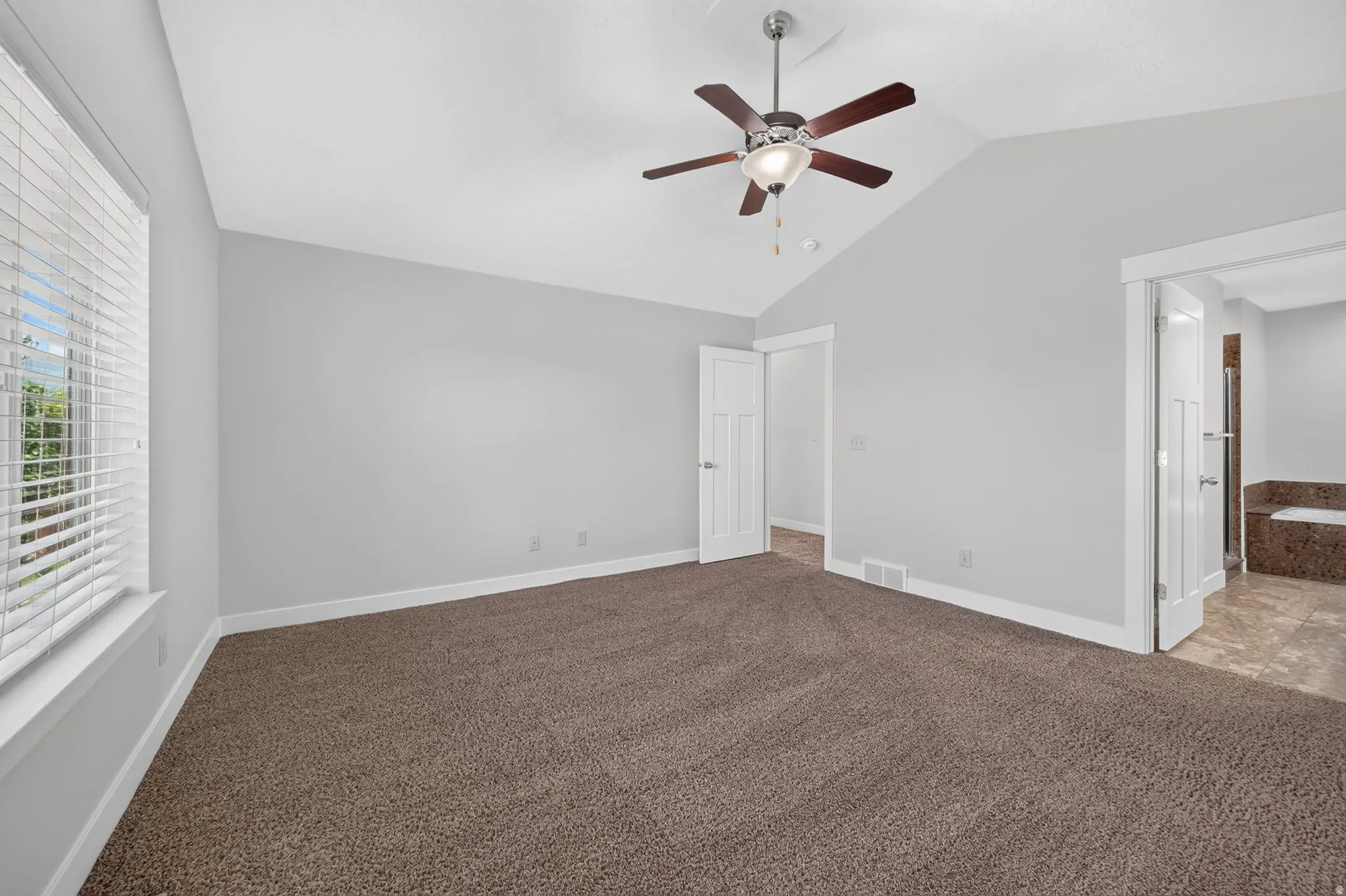 Vaulted ceiling with a ceiling fan, plush carpet flooring, white window blinds, and white interior doors