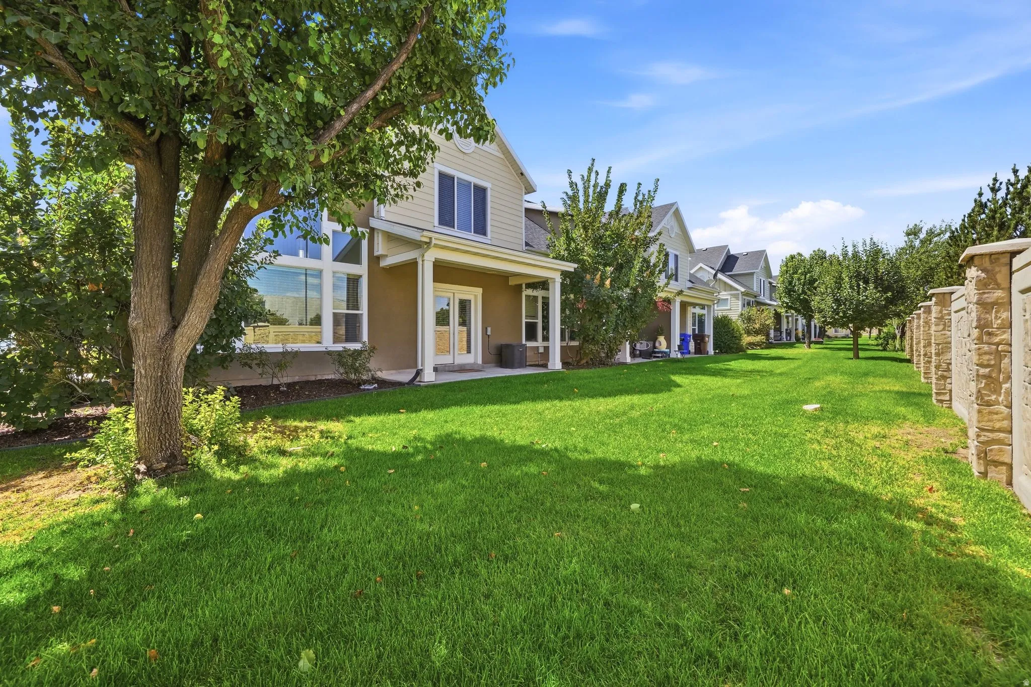 Expansive green lawn with mature trees and a stone-clad privacy wall