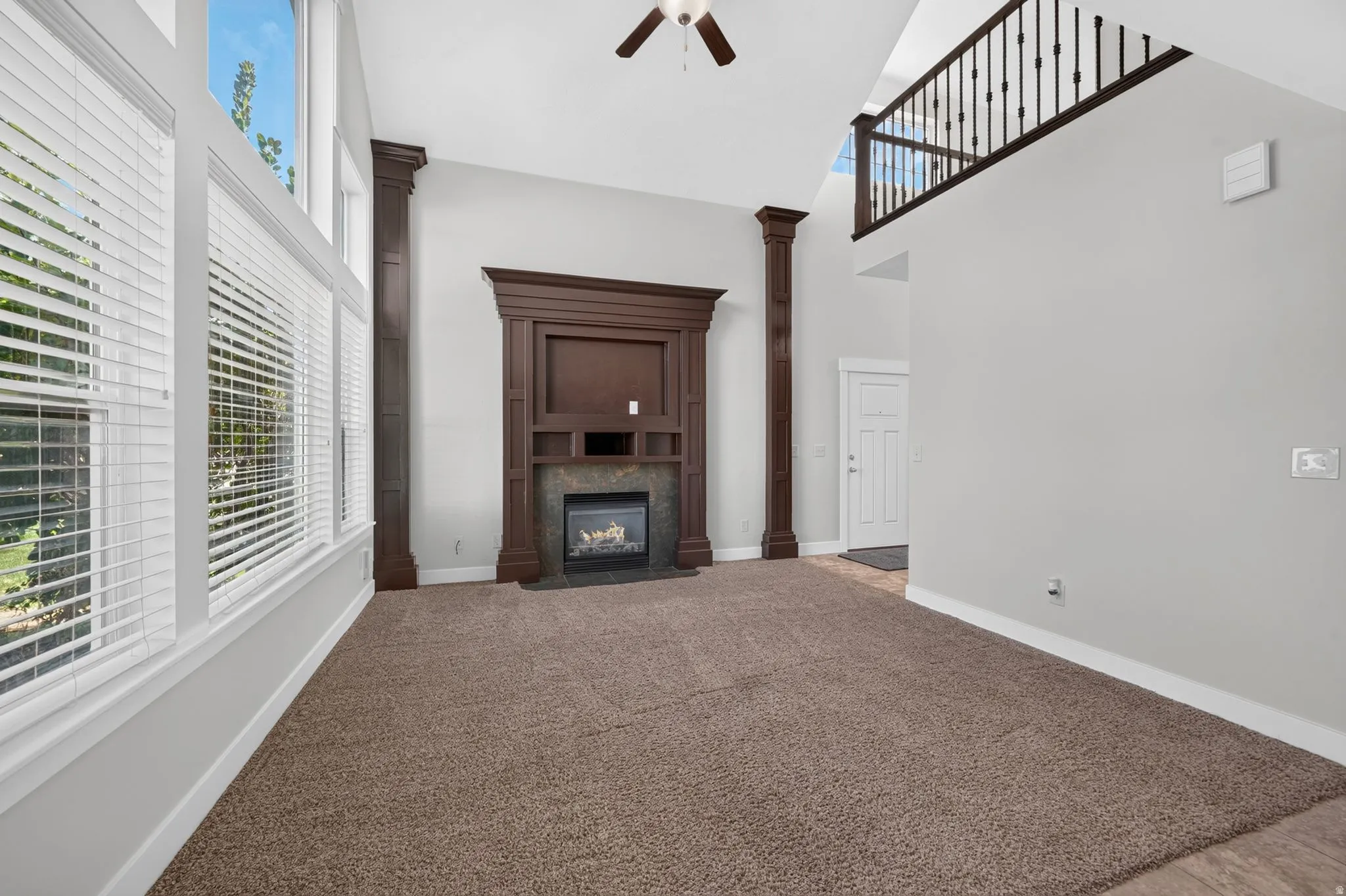 Vaulted ceiling, two-story windows, gas fireplace with stone surround, dark wood mantel, and an open upper-level railing