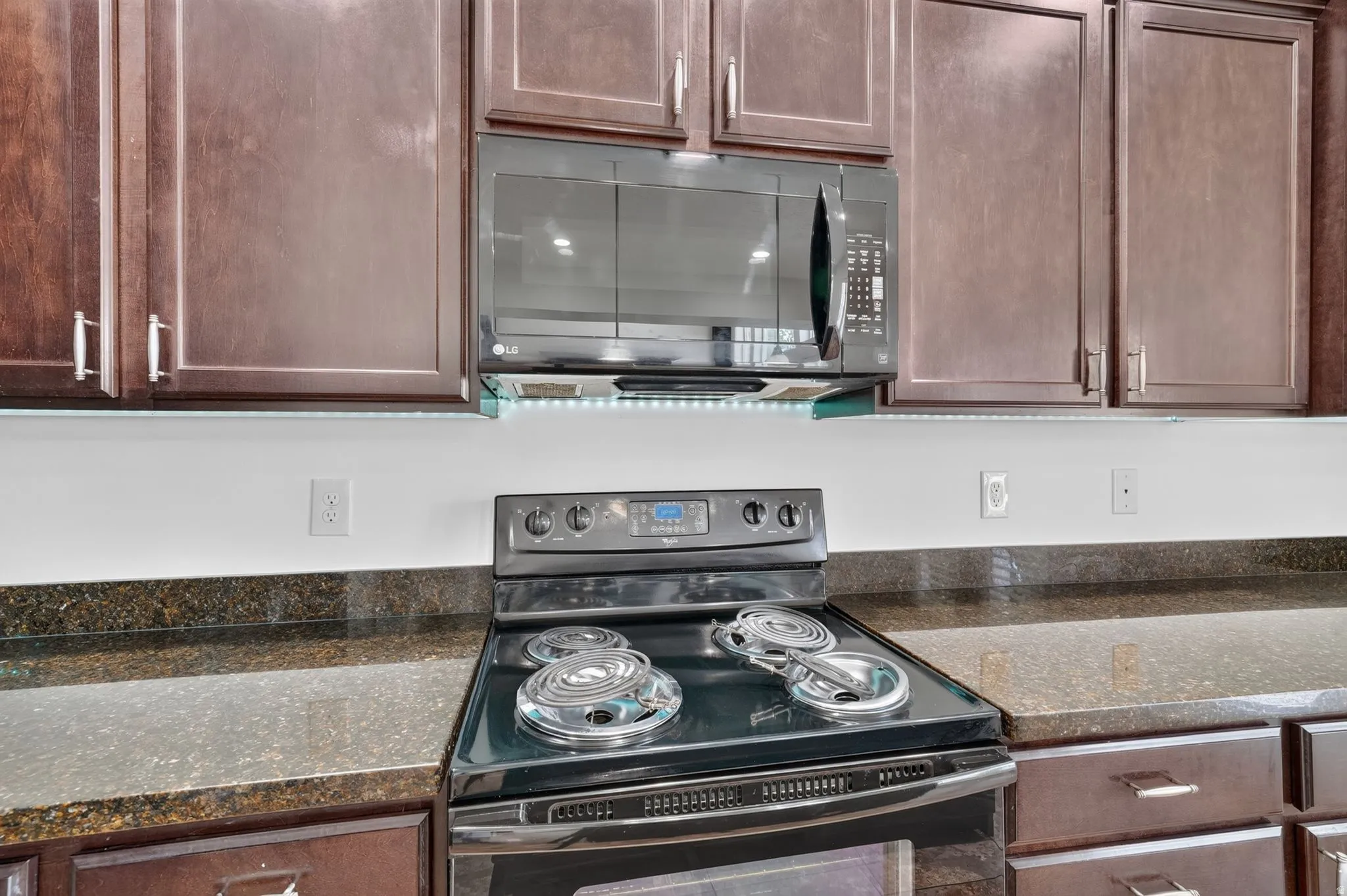 Dark wood cabinetry with brushed nickel hardware, black electric range with coil burners, and dark speckled countertops