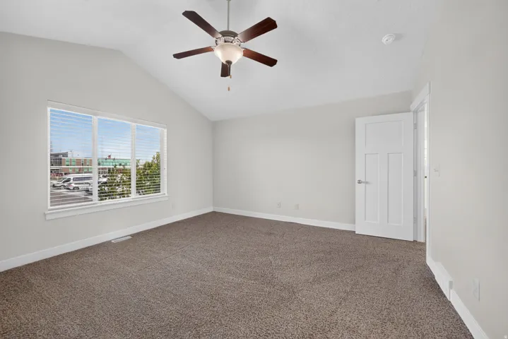 Vaulted ceiling, ceiling fan with integrated lighting, large multi-pane window, paneled interior door, and carpeted flooring