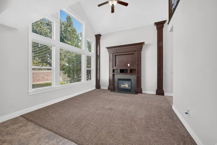 Vaulted ceiling, large windows with blinds, built-in fireplace with dark wood surround, dark wood decorative columns, and a ceiling fan