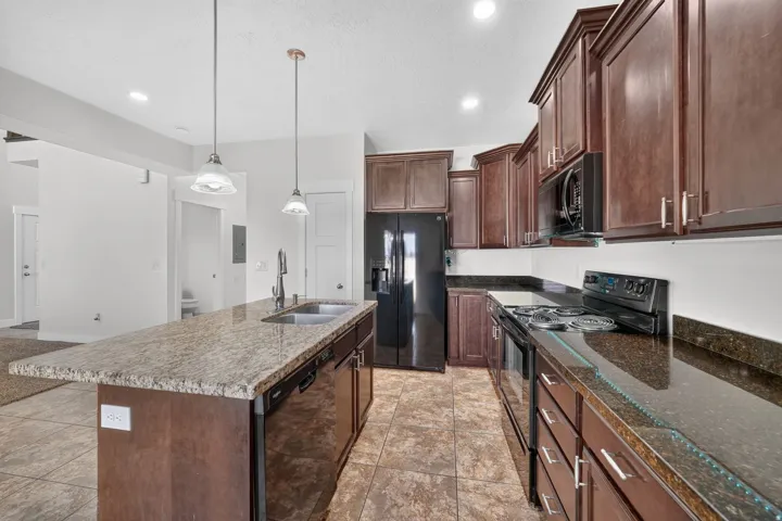 Kitchen featuring dark wood cabinetry, light-toned stone countertops, a center island with a double basin sink, stainless steel appliances, and tiled flooring