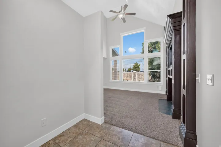 Vaulted ceiling, ceiling fan, large windows, dark wood-tone fireplace surround, and tile flooring