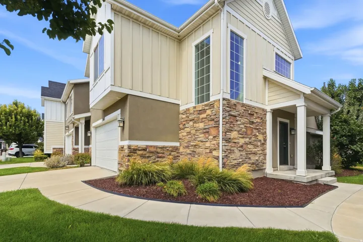 Exterior featuring stacked stone accents, vertical and horizontal siding, a covered entry porch with columns, a single-car garage, and established landscaping